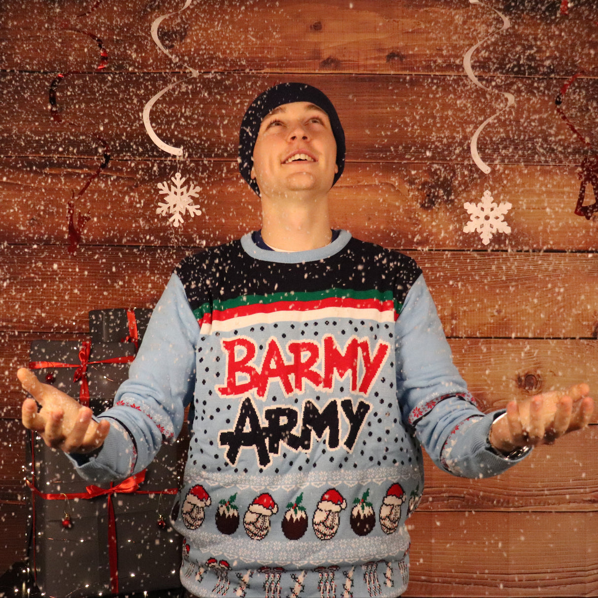 Person wearing a festive sweater with 'Barmy Army' text in front of a wooden wall.